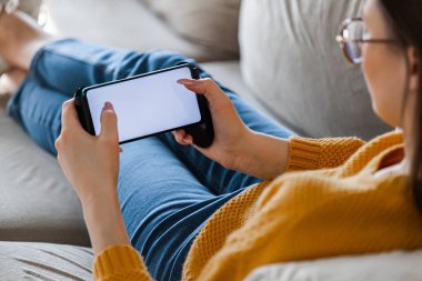 Genç bayan elinde bir cep telefonu, kanepede uzanıyor.