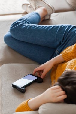 Genç bir kadın cep telefonuyla kanepede uyuyor.