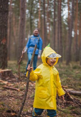 Anne ve çocuk yağmurdan sonra ormanda yürüyor. Ellerinde tahta sopalarla yağmurluklarla.