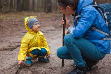 Anne ve çocuk yağmur yağdıktan sonra orman yolunda yürüyorlar, birlikte kum üzerinde ahşap sopalarla yürüyorlar.