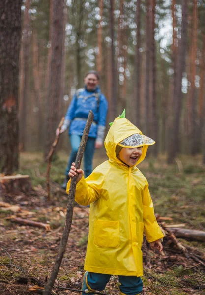 Anne ve çocuk yağmurdan sonra ormanda yürüyor. Ellerinde tahta sopalarla yağmurluklarla.