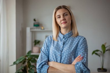 Evde duran kendine güvenen genç bir kadının portresi, kameraya bakın.