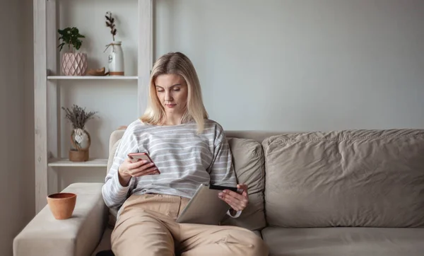 Tablet Cep Telefonu Kullanan Genç Bir Kadın Evdeki Kanepede Oturuyor — Stok fotoğraf