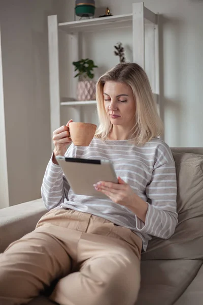 Tablet Kullanan Genç Bir Kadın Evdeki Kanepede Oturup Kahve Içiyor — Stok fotoğraf