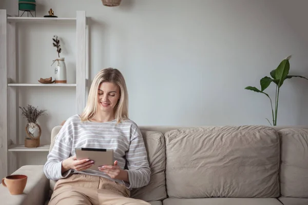 Tablet Kullanan Genç Bir Kadın Evdeki Kanepede Oturup Kahve Içiyor — Stok fotoğraf