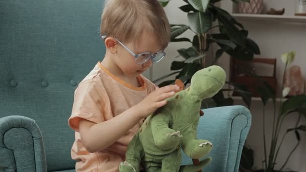 Glückliches Kind mit Brille umarmt weiches Dinosaurierspielzeug, Streicheleinheiten, Bedauern und Küsse, zu Hause — Stockvideo