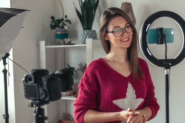 Genç kadın blogcu, kamera ayarlarının perde arkasındaki vlog için video çekmeye hazırlanıyor.