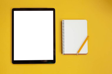Tablet screen mockup and notepad isolated on yellow background. top view