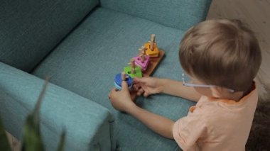 Çocuk eğitici bir oyuncak ayırıcı ile oynar, motor becerileri eğitir, evde bir koltukta oturan farklı şekil ve renkleri öğrenir