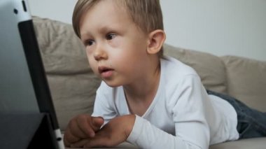 Evdeki kanepede uzanmış tablet kullanan çocuk.