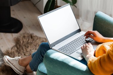 Genç bir kadın dizüstü bilgisayar kullanıyor, modellik yapıyor, evde çalışıyor.