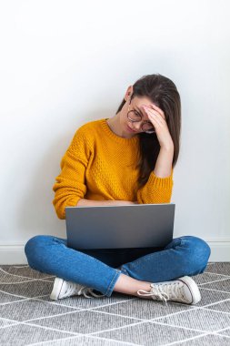 Genç bir kadın yorgun, üzgün, beyaz arka planda dizüstü bilgisayar kullanıyor.