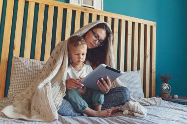 Evlerinin yatak odasında battaniyenin altında bir tabletle genç anne ve oğul.