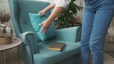 Kitap okuyan kadın evdeki koltukta oturuyor.