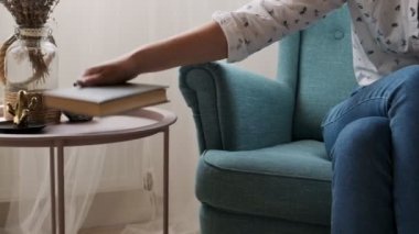 Kitap okuyan kadın evdeki koltukta oturuyor.