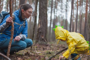 Anne ve çocuk yağmurdan sonra yağmurluklarla ormanda yürüyorlar.