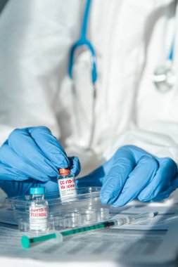 Koruyucu kıyafetli doktor ya da hemşire elinde kovid 19 aşısı ve plasebo tutuyor.