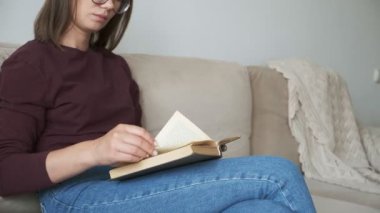 Kitap okuyan kadın evdeki kanepede oturuyor.