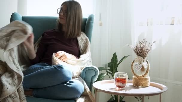 Mujer joven en gafas que cubre acogedor cuadros, sentado en sillón acogedor en casa y durmiendo — Vídeos de Stock