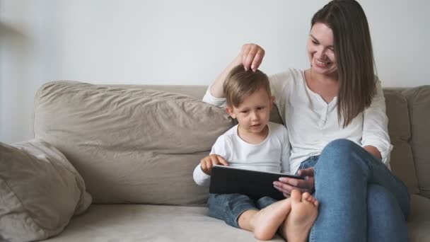 Familia madre e hijo usando la tableta sentados en el sofá en casa — Vídeos de Stock
