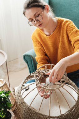 Kadın evde jüt ipten el yapımı diy lamba yapıyor.