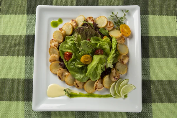 A dish of king scallop with potatoes and salad in a plate over a
