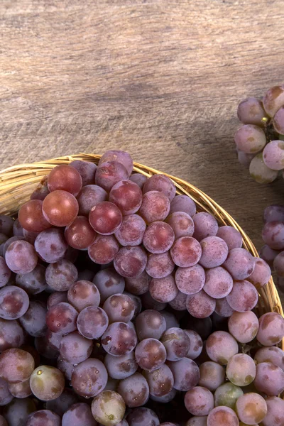 Quelques raisins rouges dans un pot en bois sur une surface en bois . — Photo