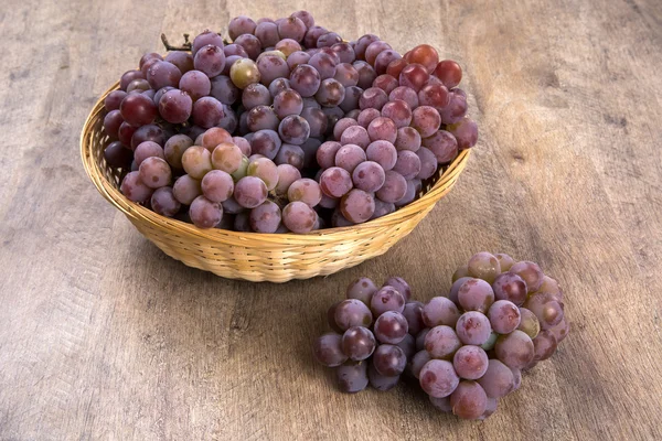 Some red grapes in a wooden pot over a wooden surface. — Stock Photo, Image