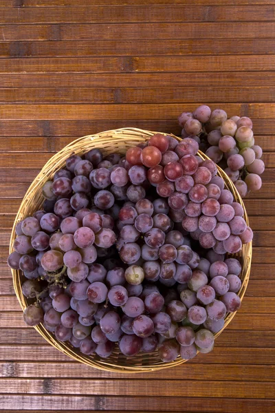 Algumas uvas vermelhas em um pote de madeira sobre uma superfície de madeira . — Fotografia de Stock