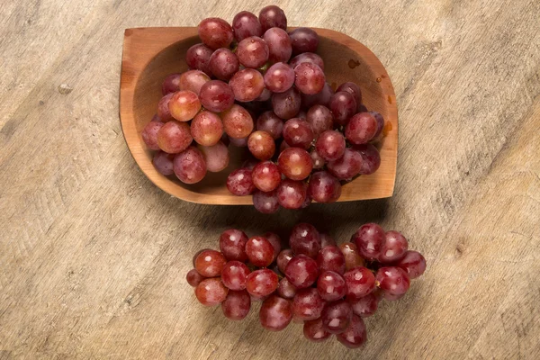 Quelques raisins rouges dans un pot en bois sur une surface en bois — Photo