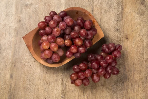 Немного красного винограда в деревянном горшке над деревянной поверхностью — стоковое фото