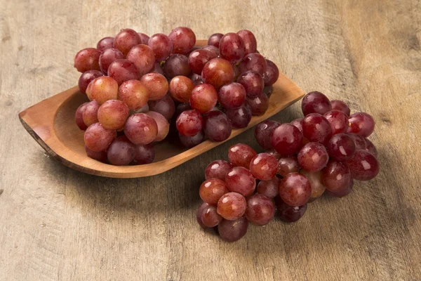 Quelques raisins rouges dans un pot en bois sur une surface en bois — Photo