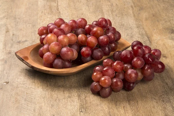 Quelques raisins rouges dans un pot en bois sur une surface en bois — Photo