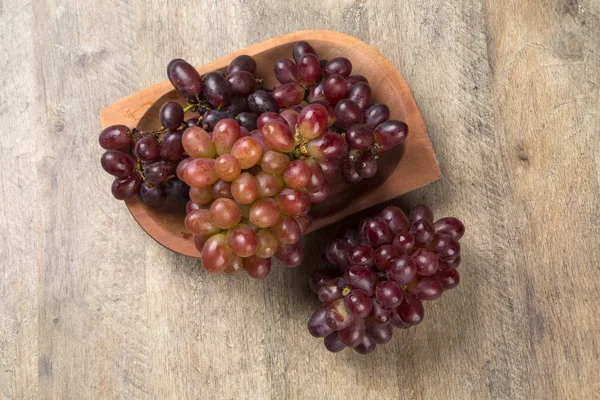 Quelques raisins rouges dans un pot en bois sur une surface en bois — Photo