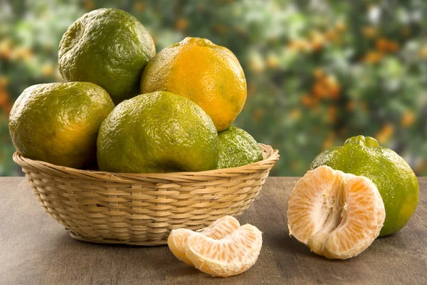 Sommige mandarijnen in een mand over een houten oppervlak — Stockfoto