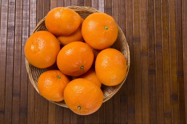Algumas tangerinas em uma cesta sobre uma superfície de madeira — Fotografia de Stock