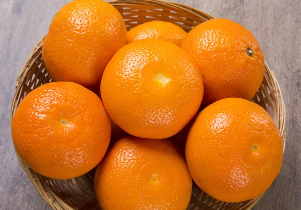 Algumas tangerinas em uma cesta sobre uma superfície de madeira — Fotografia de Stock