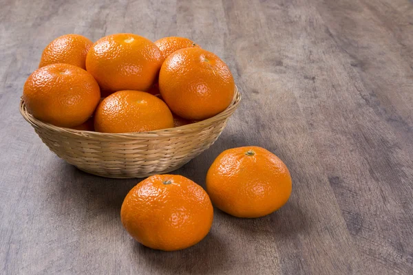 Algumas tangerinas em uma cesta sobre uma superfície de madeira — Fotografia de Stock