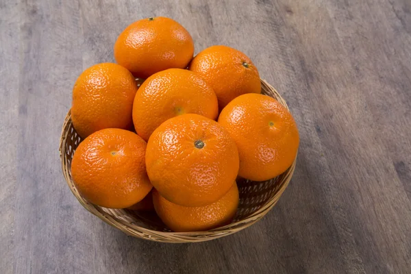 Algumas tangerinas em uma cesta sobre uma superfície de madeira — Fotografia de Stock