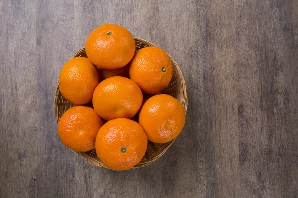 Algumas tangerinas em uma cesta sobre uma superfície de madeira — Fotografia de Stock