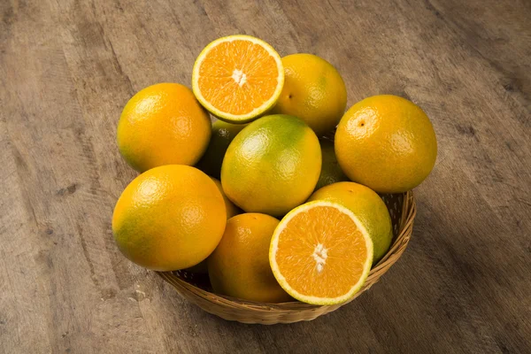 Close up van sommige sinaasappelen in een mand over een houten oppervlak — Stockfoto