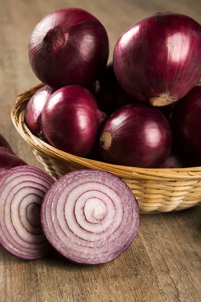 Red onions in a basket and a cut red onion over a table.