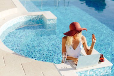 Laptop kullanan ve havuz kenarında çalışan bir kadın.