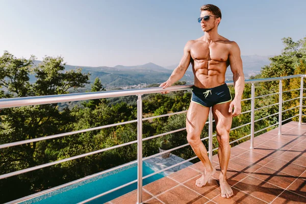 Moteportrett av en muskuløs mann i badebukse ved svømmebassenget – stockfoto