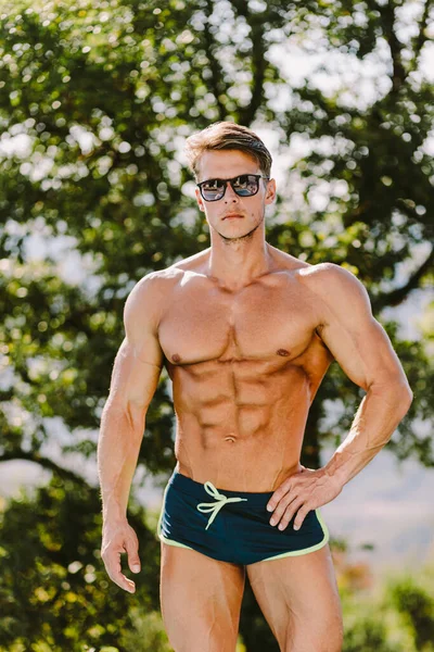 Ritratto di un uomo muscoloso in costume da bagno e occhiali da sole — Foto Stock
