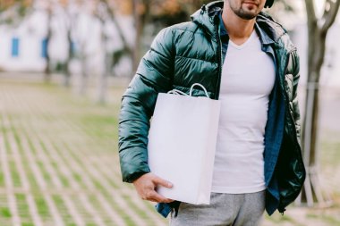 Beyaz kağıt çanta ve beyaz tişört modeli tutan bir adam.