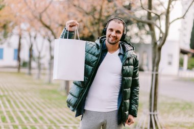 Beyaz kağıt çanta ve beyaz tişört modeli tutan bir adam.