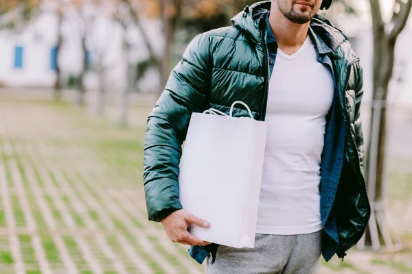 Beyaz kağıt çanta ve beyaz tişört modeli tutan bir adam.