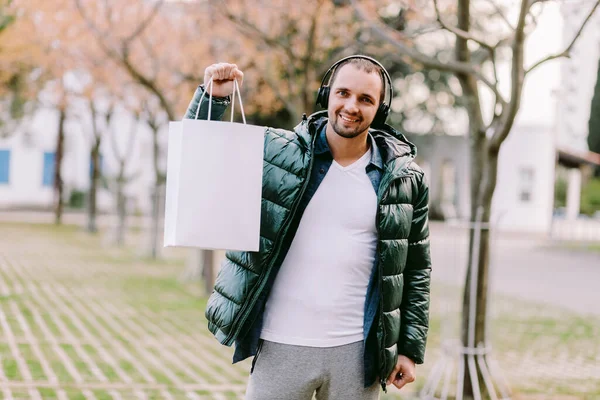 Beyaz kağıt çanta ve beyaz tişört modeli tutan bir adam.