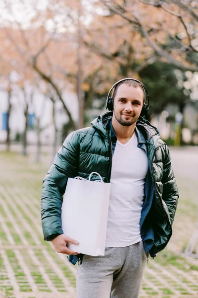 Beyaz kağıt çanta ve beyaz tişört modeli tutan bir adam.